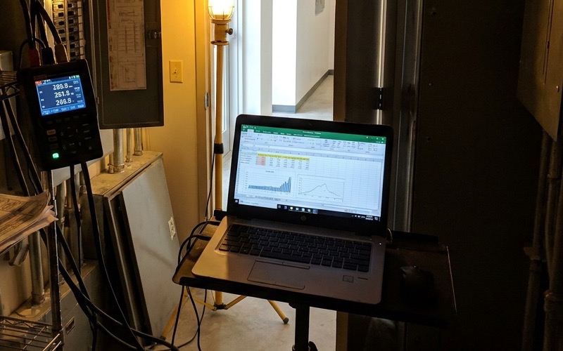 Power meter and laptop showing electrical demand charts in a building electrical room